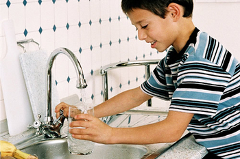 Junge mit einem Glas Wasser aus dem Wasserhahn